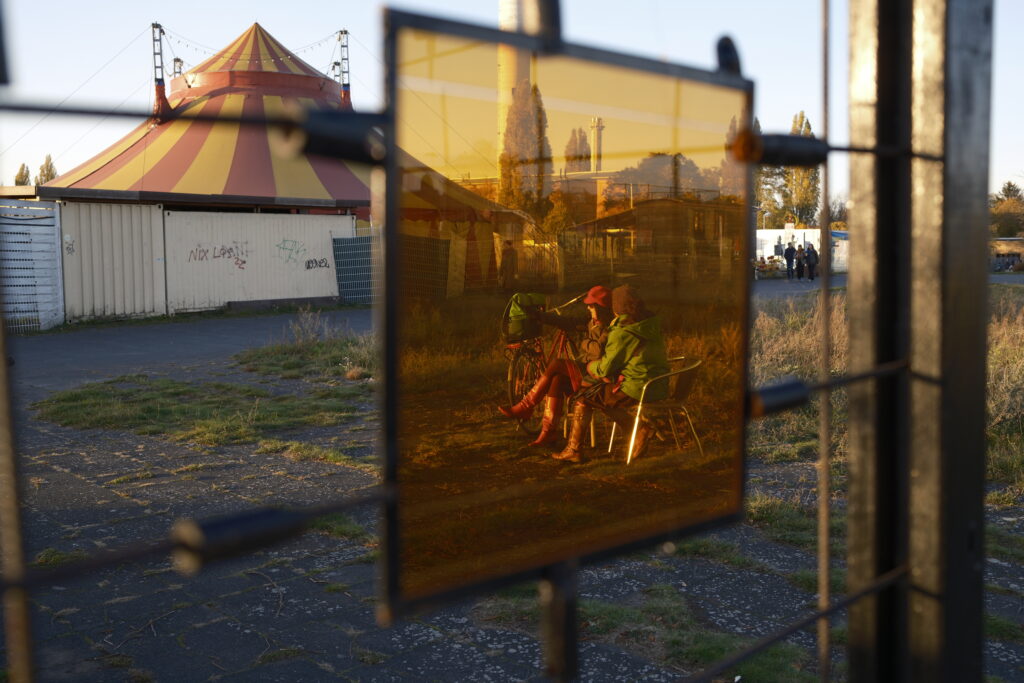 Zwei Personen, die auf dem Tempelhofer Feld in Berlin sitzen und durch ein farbiges Glas fotografiert werden.