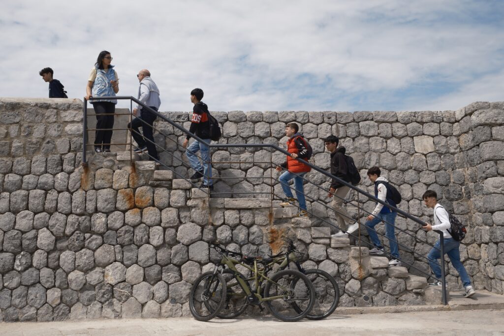 Jugendliche und Erwachsene steigen eine Steintreppe auf der Mole von Cefalu hinauf, davor stehen Fahrräder