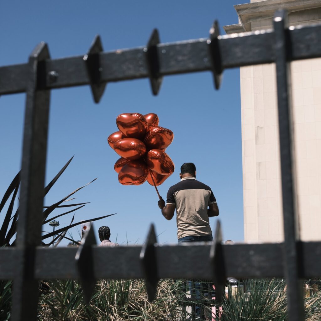 Person mit Luftballons in Herzform vor einem blauen Himmel.