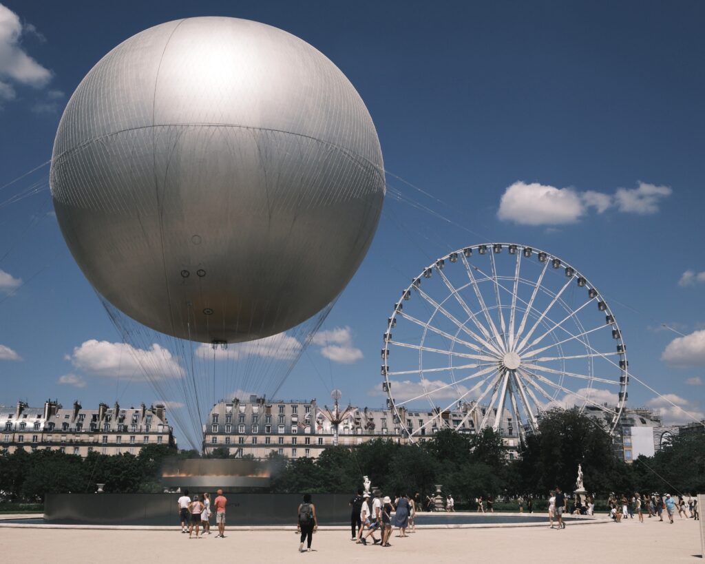 Ein Heißluftballon und ein Riesenrad vor blauem Himmel im Garten vor dem Louvre.