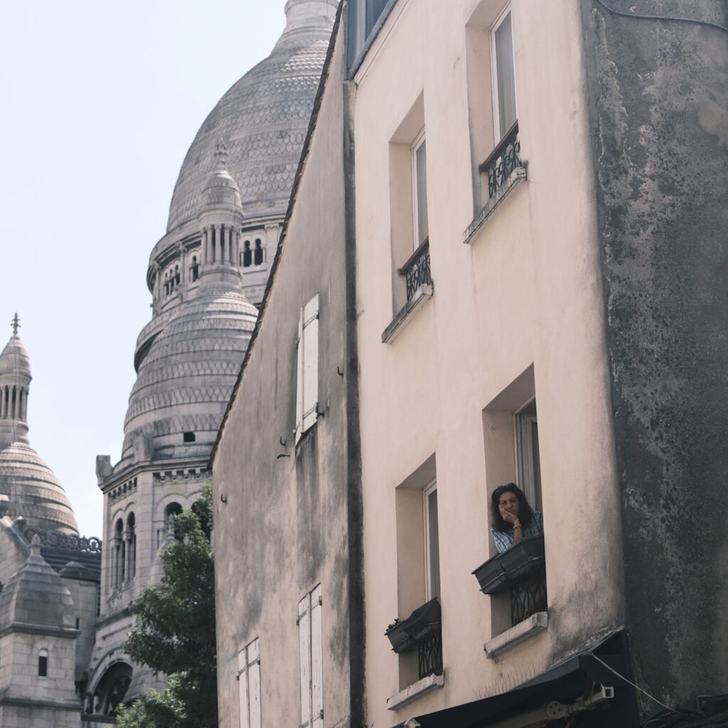 Montmartre-Haus mit Fensterläden im Vordergrund, im Hintergrund erhebt sich die Kuppel der Basilika Sacré-Cœur.