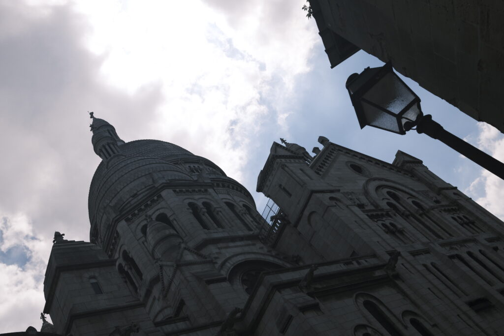 Ungewöhnliche Perspektive auf die Kuppeln der Basilika Sacré-Cœur und eine Pariser Straßenlaterne, fotografiert gegen den Himmel.