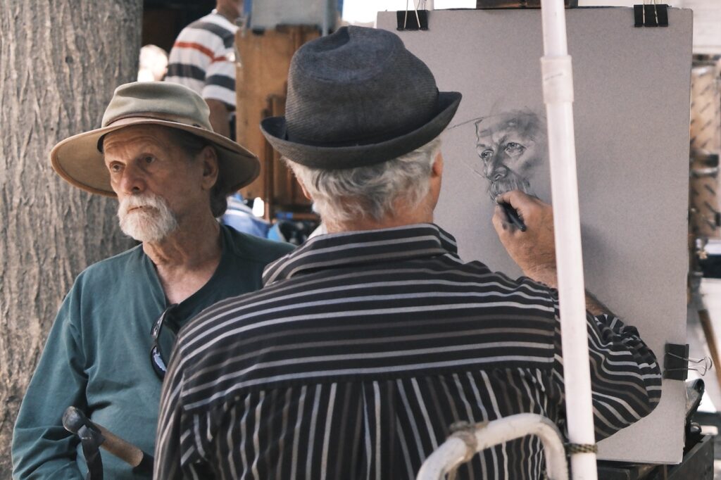 Künstler zeichnet im Freien auf dem Place du Tertre in Montmartre, mit Passanten und Gemälden im Hintergrund.