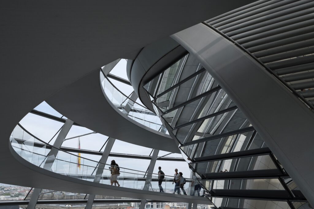 Menschengruppe auf der spiralförmigen Rampe in der Glas- und Stahlkuppel des Reichstags, Linien und Lichtführung bestimmen das Bild.