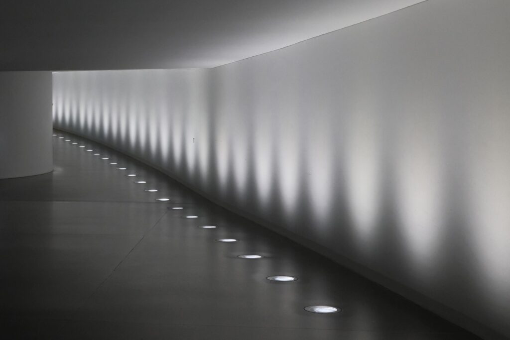 Minimalistischer, abgedunkelter Flur im Bundestag mit weißer Wand, indirekter Beleuchtung und Bodenlichtern.